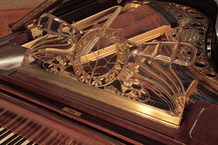 Bluthner music desk is in a butterfly shape made from bevelled glass and an intricate metal filigree design. A central circular tree of life is surrounded by a laurel leaf wreath. Whiplash lines and stylised foliage and flowers complete the design.