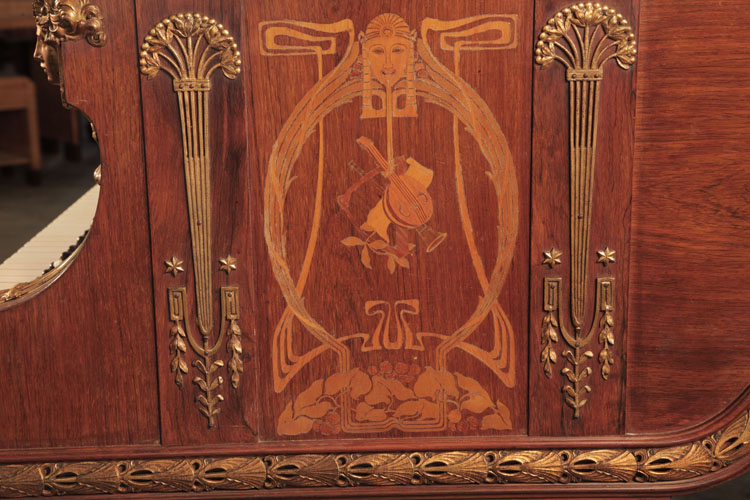 The piano cheek side panel is inlaid with an Art Nouveau design featuring a stylised female head surrounded by whiplash lines and foliage. Musical instruments sit centrally in the design. Columnar, Empire style gilt mounts stand each side of the inlay. Napoleonic emblems of stars, palmettes and foliage feature here