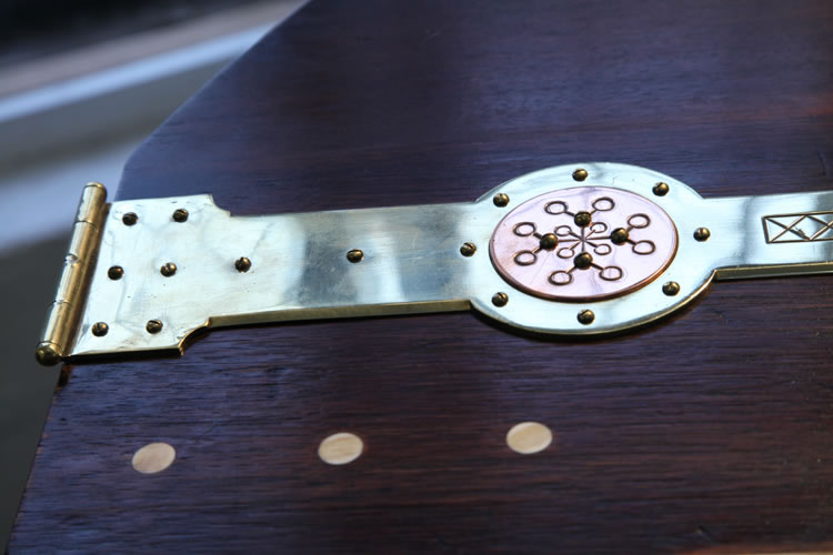 Arts and Crafts objects were simple in form, without superfluous or excessive decoration, and how they were constructed was often still visible. Here the hinges, often hidden in modern furniture, are a strong element of the piano's design. The hinges are large and stamped with a circular design. Returning to Norse mythology, this symbol appears to depict the nine worlds, a symbol of Norse cosmology. 