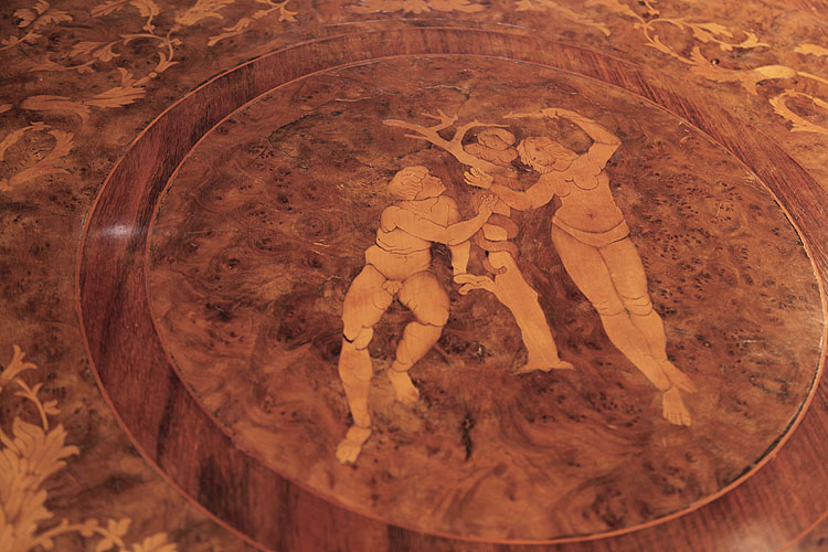Piano lid circular motif featuring an Eden inspired design of a nude male and female figure with a serpent on a tree 