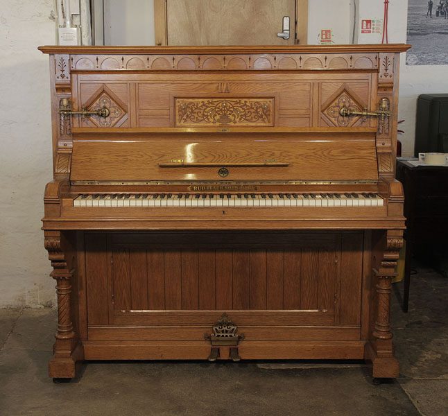 An 1895, English Gothic style, Ibach upright piano with a carved, oak case and ornate brass candlesticks and handles. Cabinet features traditional folk art motif carvings..